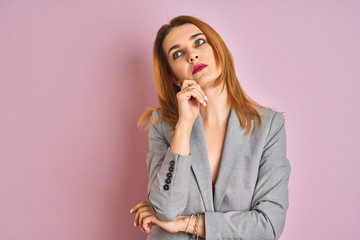 Young caucasian business woman wearing a suit over isolated pink background with hand on chin thinking about question, pensive expression. Smiling with thoughtful face. Doubt concept.
