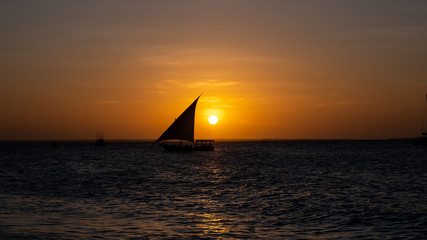 Sunset on a beach in Zanzibar with a boat silhouette in the sun	