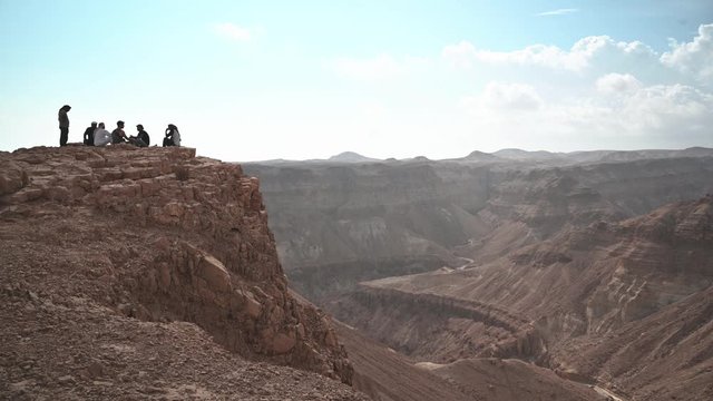 Group of people sit on the edge of Desert Cliff. Israel. NIK_6258-02