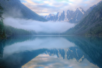 Misty morning on a mountain lake. High mountains with glacier, cold lake and fog. Thick fog swirls over the water.