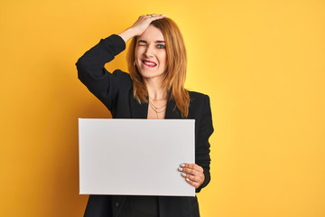 Naklejka premium Redhead business caucasian woman holding banner over yellow isolated background stressed with hand on head, shocked with shame and surprise face, angry and frustrated. Fear and upset for mistake.