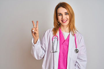 Redhead caucasian doctor woman wearing pink stethoscope over isolated background showing and pointing up with fingers number two while smiling confident and happy.