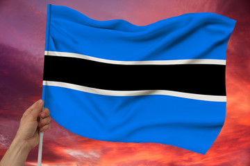 hand holds against the background of the sky with clouds the colored flag of Botswana on the...