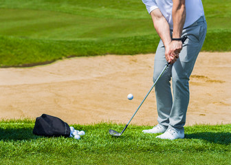 Golf coach hitting ball on sand trap.