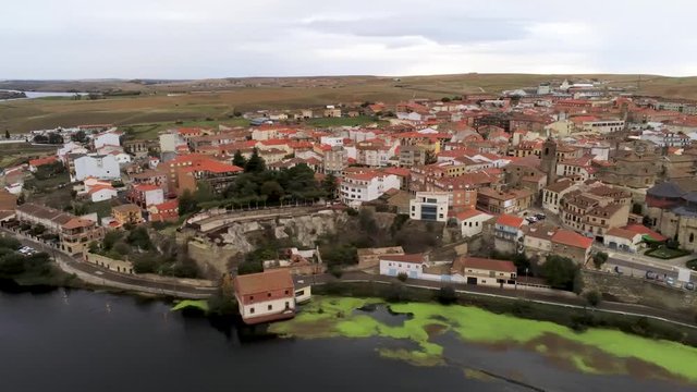 Beautiful aerial panoramic view of historic city Alba de Tormes, Castilla y Leon region, Spain. Ancient city on riverfront in a cloudy day. Drone pan from right to left