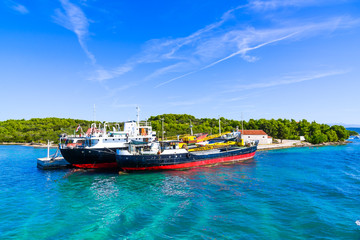 Fototapeta premium Kornati, Dalmatia. Commercial cargo ship in the port, industrial ships on the sea, transport and logistic concept. Boats in the harbor at the blue lagoon at the island, Adriatic Sea, Croatia.