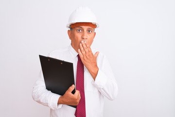 Senior architect man wearing security helmet holding clipboard over isolated white background cover mouth with hand shocked with shame for mistake, expression of fear, scared in silence, secret