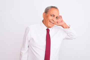 Senior grey-haired businessman wearing elegant tie over isolated white background smiling with hand over ear listening an hearing to rumor or gossip. Deafness concept.