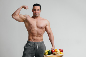 Sexy vegan guy with a naked torso posing in the Studio next to fruit. Diet. Healthy diet