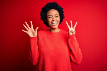 Young beautiful African American afro woman with curly hair wearing casual sweater showing and pointing up with fingers number eight while smiling confident and happy.