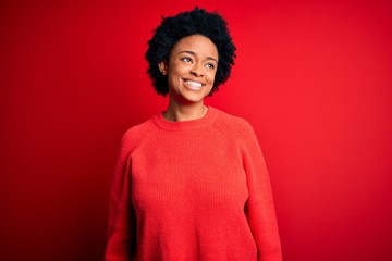 Young beautiful African American afro woman with curly hair wearing casual sweater looking away to side with smile on face, natural expression. Laughing confident.