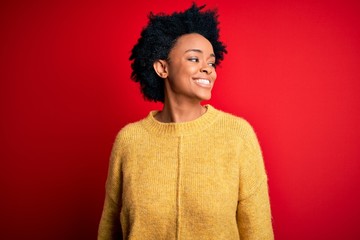 Young beautiful African American afro woman with curly hair wearing casual yellow sweater looking away to side with smile on face, natural expression. Laughing confident.
