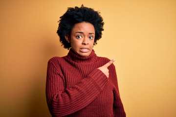 Fototapeta na wymiar Young beautiful African American afro woman with curly hair wearing casual turtleneck sweater Pointing aside worried and nervous with forefinger, concerned and surprised expression