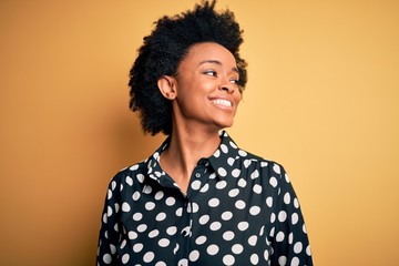 Fototapeta na wymiar Young beautiful African American afro woman with curly hair wearing casual shirt standing looking away to side with smile on face, natural expression. Laughing confident.