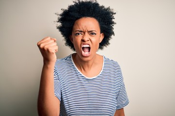 Young beautiful African American afro woman with curly hair wearing striped t-shirt angry and mad raising fist frustrated and furious while shouting with anger. Rage and aggressive concept.