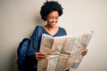 Young African American afro tourist woman with curly hair wearing backpack using city map with a happy face standing and smiling with a confident smile showing teeth