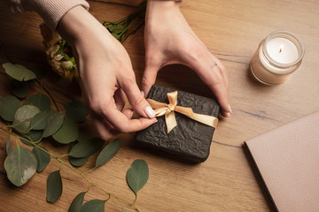 Girl packs a gift.  Female hands prepare a gift on a wood background with a flowers and candles....
