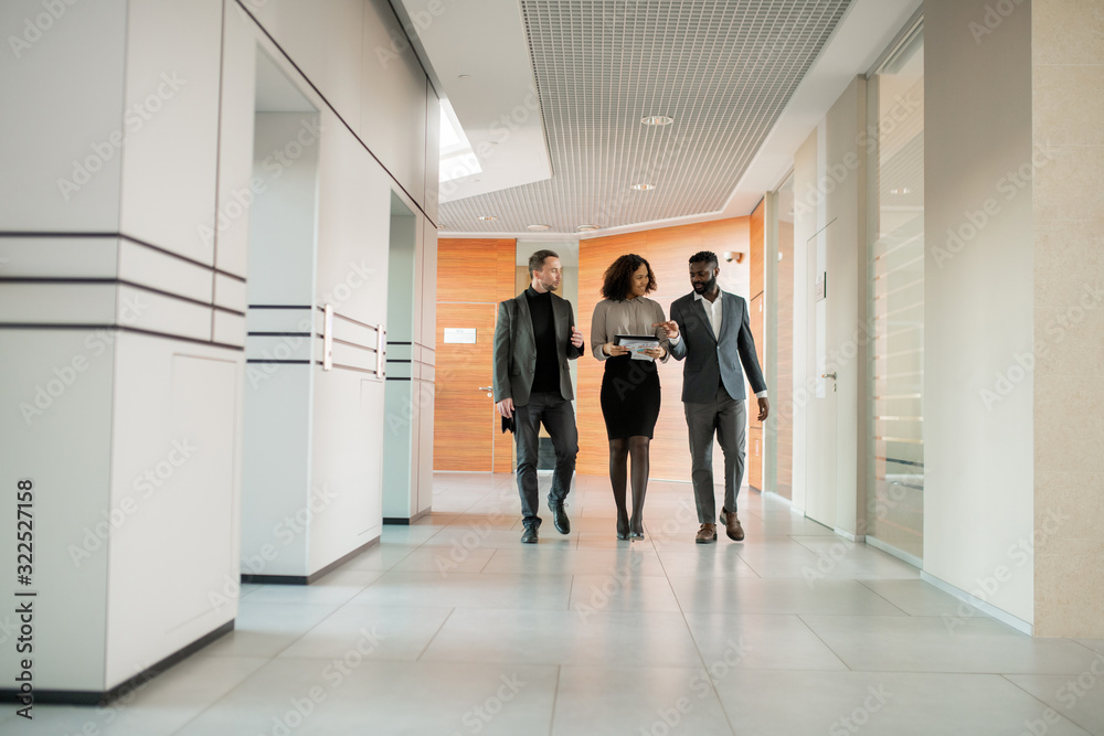 Poster interracial business colleagues walking along corridor and discussing project on move