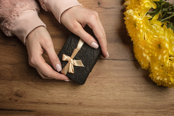  Girl packs a gift.  Female hands prepare a gift on a wood background with a  yellow flowers....