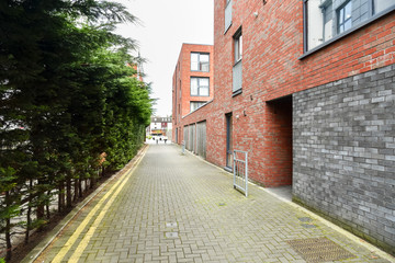 Fototapeta na wymiar Deserted cobbled Path alongs a modern brick apartment building on a cloudy spring day