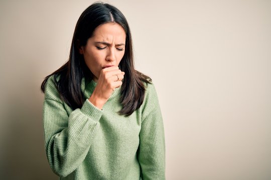 Young brunette woman with blue eyes wearing turtleneck sweater over white background feeling unwell and coughing as symptom for cold or bronchitis. Health care concept.