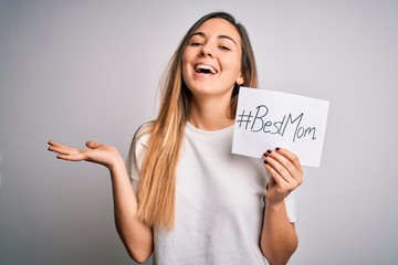 Young beautiful woman holding paper with best mom message celebrating mothers day very happy and excited, winner expression celebrating victory screaming with big smile and raised hands
