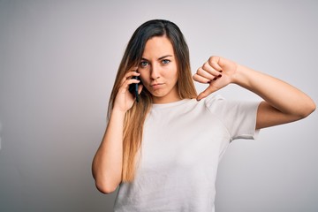 Young beautiful brunette woman having conversation talking on the smartphone with angry face, negative sign showing dislike with thumbs down, rejection concept