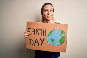 Young beautiful woman holding banner asking for earth and enviroment conservation serious face...