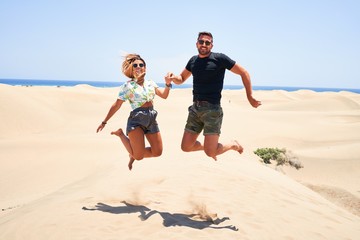 Young beautiful couple smiling happy and confident. Jumping with smile on face at the beach
