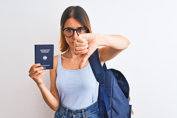 Beautiful redhead student woman wearing backpack and holding passport of germany with angry face, negative sign showing dislike with thumbs down, rejection concept