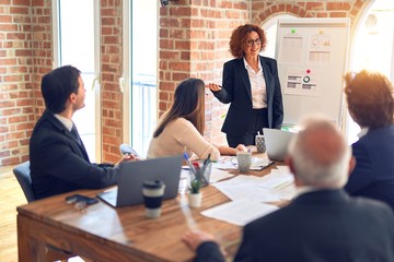 Group of business workers smiling happy and confident in a meeting. Working together looking at presentation using board and charts at the office.