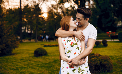 A young couple posing in a beautiful park have just found out that their family will become bigger in some months