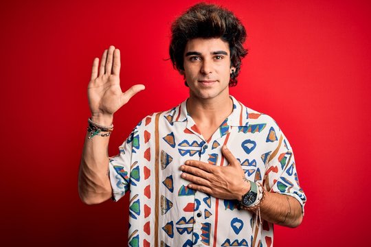 Young handsome man on vacation wearing summer shirt over isolated red background Swearing with hand on chest and open palm, making a loyalty promise oath