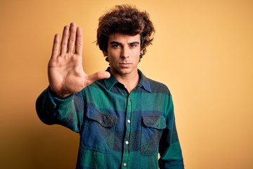 Young handsome man wearing casual shirt standing over isolated yellow background doing stop sing...