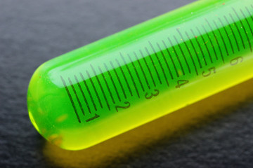 Bright green fluorescent substance in a measuring tube, on a black background. Macro photography.