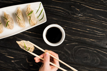 cropped view of woman eating delicious Chinese boiled dumpling with chopsticks and soy sauce at...