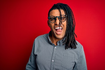 Young handsome african american man with dreadlocks wearing casual shirt and glasses winking...