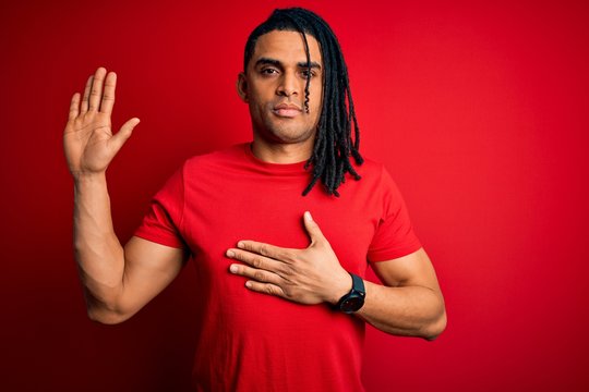 Young handsome african american afro man with dreadlocks wearing red casual t-shirt Swearing with hand on chest and open palm, making a loyalty promise oath
