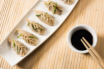 top view of delicious Chinese boiled dumplings on plate near chopsticks and soy sauce on bamboo mat