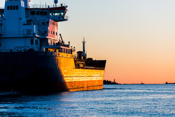 Large cargo ship at sunset, close-up. Lighthouse in the background. Riga, Latvia