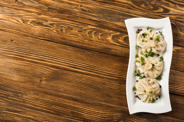 top view of delicious Khinkali with cilantro on plate on brown wooden table