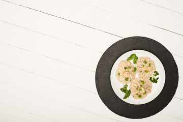 top view of delicious Khinkali with cilantro on plate on white wooden table