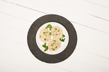 top view of delicious Khinkali with cilantro on plate on white wooden table