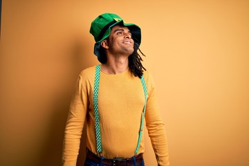 Fototapeta premium Young african american man wearing green hat celebrating saint patricks day looking away to side with smile on face, natural expression. Laughing confident.