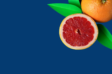 Juicy grapefruits with green leaves from paper isolated on blue background with copy space. Creative summer composition