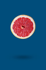 Flying grapefruit fruit with soft shadow on blue background. Trendy creative minimal food concept