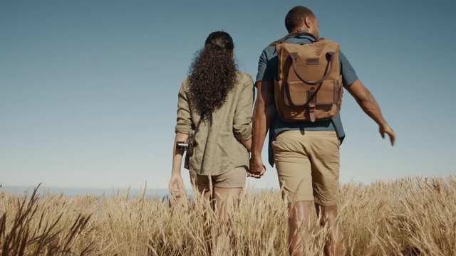 Rear view of couple walking through a dry grass field. Young man and woman hiking together in nature.