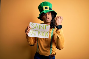 Young african american man wearing green hat holding banner celebrating saint patricks day annoyed and frustrated shouting with anger, crazy and yelling with raised hand, anger concept