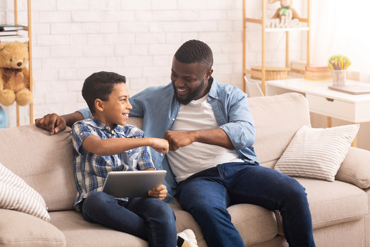 Afro father and son bumping fists, celebrating victory with digital tablet