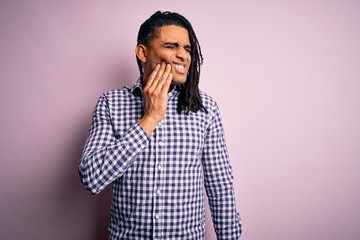 Young handsome african american afro man with dreadlocks wearing casual shirt touching mouth with hand with painful expression because of toothache or dental illness on teeth. Dentist